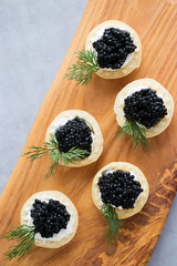 Tartlets with black caviar on wooden board.