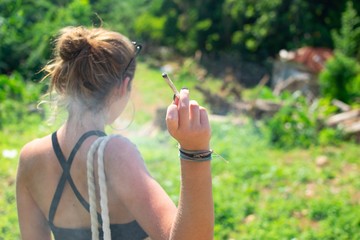 Female smoking a marijuana joint shot from behind - obrazy, fototapety, plakaty