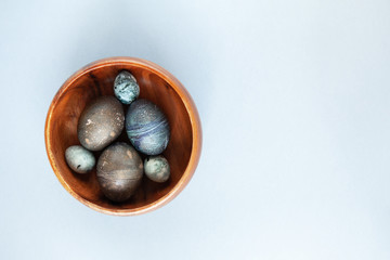 Creatively painted chicken and quail Easter eggs with natural hibiscus dye, look like sea stones in bowl on gray background, copy space. Happy Easter DIY concept. Soft slective focus. Flat lay
