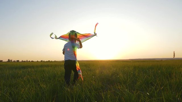 A boy runs across the field at sunset with a kite flying over his head. A chidhood dream. Kids Games
