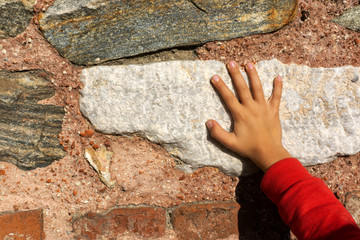 little boy is touching stone wall with his hand