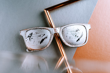 Summer glasses silver color with scratches on a gray copper paper geometric background with a metal gold frame and reflection in the mirror
