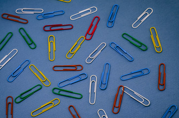 heap of multicolored paperclips scattered on a blue background