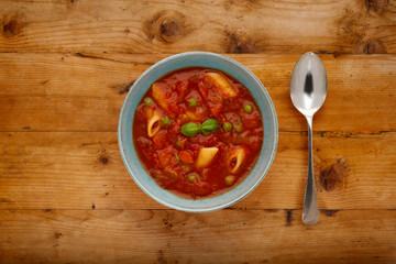 A bowl of delicious minestrone soup, topped with a sprig of basil, in a rustic bowl, on a wooden background, with a silver spoon.
