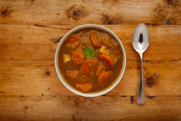 A bowl of delicious hearty winter vegetable soup, in a rustic bowl, on a wooden background, with a silver spoon.