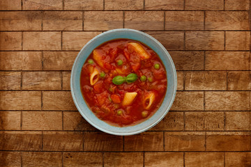 A bowl of delicious minestrone soup, topped with a sprig of basil, in a rustic bowl, on a checked wooden background.