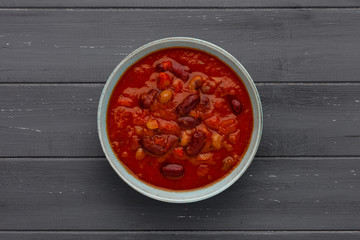 A bowl of delicious chilli bean soup, in a rustic bowl, on a distressed wooden background, with space for copy.
