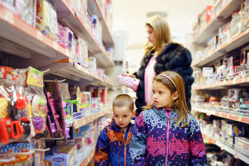 Mother woman and her son and daughter children between the shelves at the shopping mall