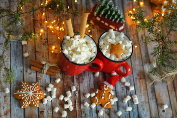 cocoa or hot chocolate with marshmallow on rustic table. Christmas or New Year composition. Gingerbread man with candy cane. Close view of marshmallow in red cup with sparkler. soft selective focus.