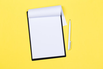 Clipboard with white sheet and pen on a yellow background. View from above. space for text