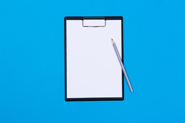 Clipboard with white sheet and pen on a blue background. View from above. space for text