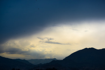 Small silhouettes of birds in flight at the end of the afternoon with mountains background