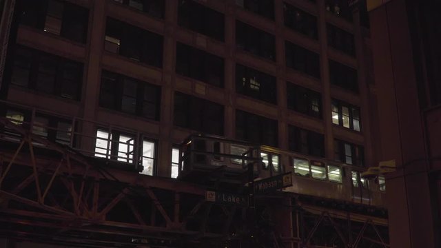 Typical Chicago night time establishing shot of generic downtown urban apartment building along loop train tracks as trains pass by outside loft windows