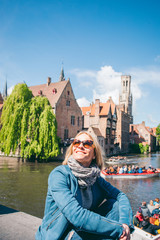 Fototapeta premium A beautiful young girl sits on the background of a famous tourist spot with a canal in Bruges, Belgium
