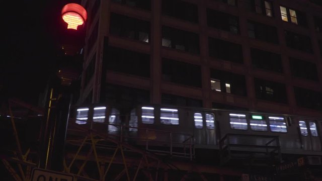 Typical Chicago night time establishing shot of generic downtown urban apartment building along L train tracks as trains pass by outside loft windows and intersection traffic light changes green