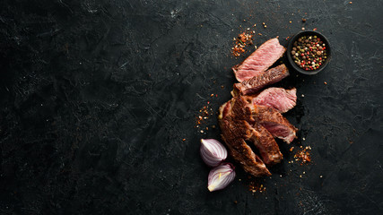 Sliced grilled steak on black stone background. Black Angus. Top view. free space for your text. Rustic style.