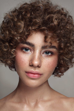 Portrait of young beautiful freckled girl with curly hair and clean makeup