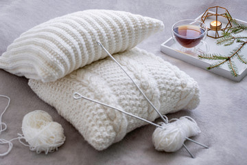 Obraz na płótnie Canvas Cozy knitting set with white yarn and knitting needles with tea in the background