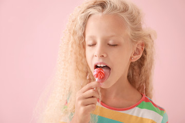 Cute little girl with lollipop on color background