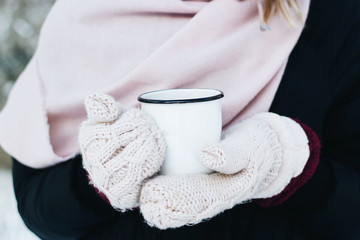 Female holding a mug of tea on winter picnic in the woods. Woman hand`s in a warm pink knitted gloves