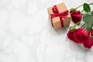 Present with pink ribbon and roses on marble background with copyspace. Minimalistic composition for the holidays.