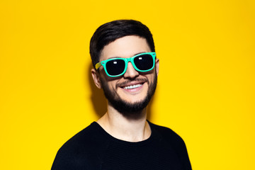 Studio portrait of young smiling man wearing sunglasses on yellow background.