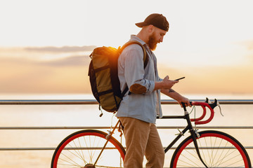 young bearded man traveling on bicycle at sunset sea