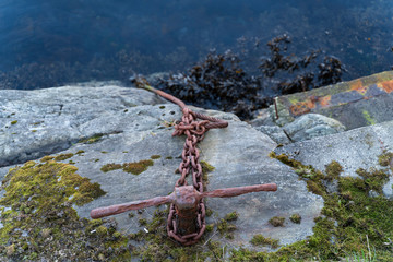 rusty purple anchor chain on a mossy stone leading into the dark water with algae in norway, Alesund