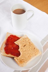 Peanut butter and jam on slices of bread with cup of coffee