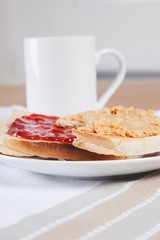 Peanut butter and jam on slices of bread with cup of coffee