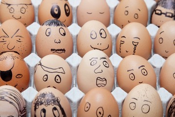 Funny faces on painted on brown eggs arranged in carton