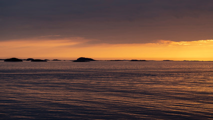 colorful orange sunset under dark sky over the sea above the arctic circle in norway shot from a boat with a view oves of Norway on a sunny day in spring within a beautiful landscape shot from a boat 