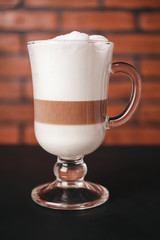 Glass with latte macchiato coffee on dark table, brick wall background
