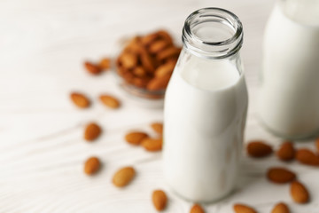 Close-up of almond milk in reusable glass bottles, almond nuts on a white wooden table lie nearby.