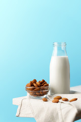 Glass reusable bottle with almond milk, almond nuts lie nearby, textile napkin on a white wooden table and a blue background.