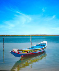 Traditional colorful wooden boat on the river in sea lagoon and a beautiful sky in the background, Africa, Senegal.