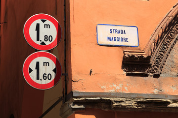 Fototapeta premium Height and width limitation mandatory traffic signs on a narrow side street in the old town of Bologna, Italy, Europe. Name plate of Strada Maggiore (Main street) on the wall.