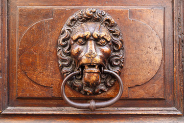 Lion's head carved in wood bearing a metal door knocker in his jaw. In the old town of Geneva, Switzerland.