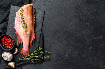 Raw red sea perch on a stone Board with thyme. Black background. Top view. Space for text