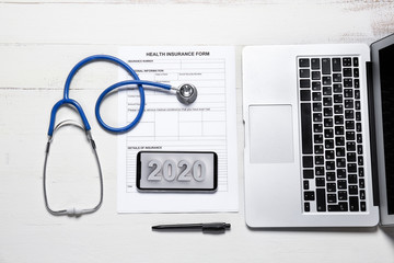 Laptop, stethoscope, mobile phone and health insurance form on white table