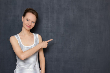Portrait of happy friendly young woman pointing at copy space on right