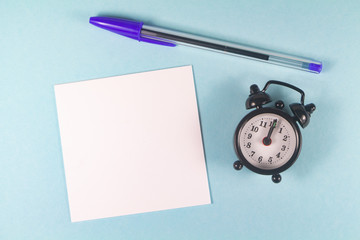 Pen, paper and black alarm clock on blue background