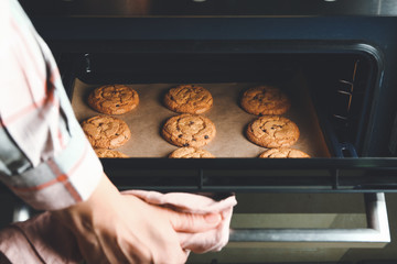 Woman taking baking tray with cookies out of oven - Powered by Adobe