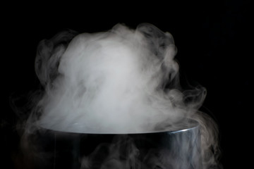 Puffs of white smoke randomly rising rise from the chimney partially flowing down its edges on a black background