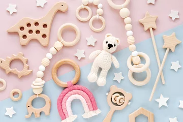 Fototapeten Cute wooden baby toys on pink and light-blue background. Knitted bear, rainbow, dinosaur toy, beads and stars. Eco accessories,  beanbag and teethers for newborn. Flat lay, top view © igishevamaria