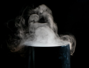 Puffs of white smoke randomly rising rise from the chimney partially flowing down its edges on a black background