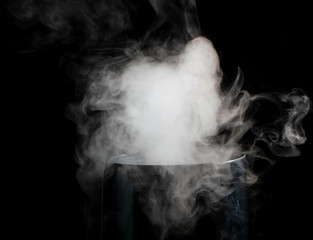 Puffs of white smoke randomly rising rise from the chimney partially flowing down its edges on a black background
