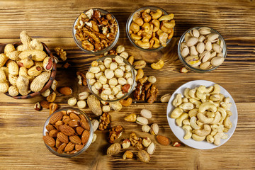 Assortment of nuts on wooden table. Almond, hazelnut, pistachio, peanut, walnut and cashew in small bowls. Top view. Healthy eating concept