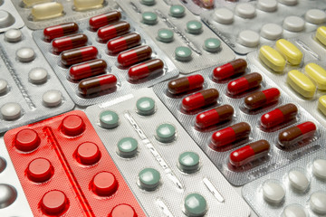 Multi-colored tablets, capsules and vitamins in blister packs arranged in a background