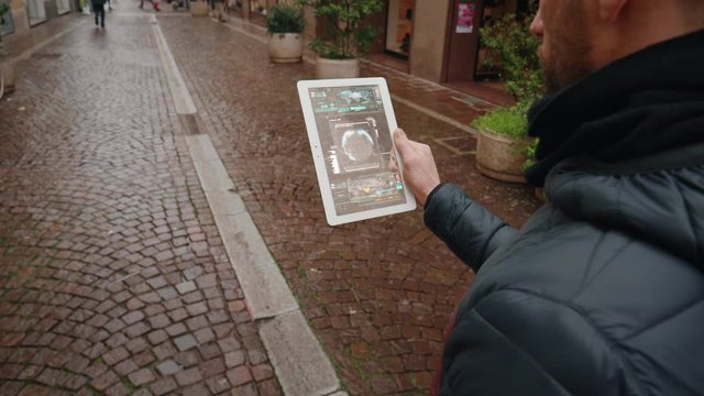 Close up of an young man is using a futuristic latest innovative technology glass tablet with augmented reality holograms during walking in city center by day.